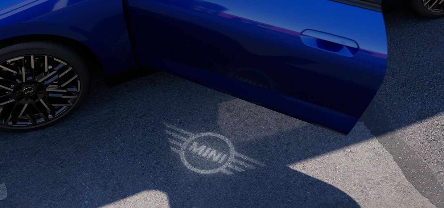 Exterior view of all-electric MINI Cooper with open door and MINI logo welcome light on the ground